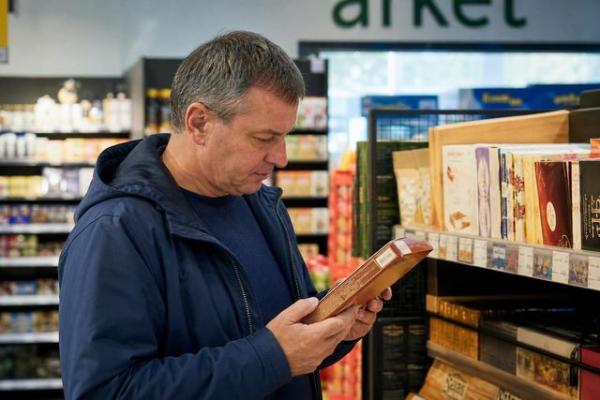 Покупатель внимательно изучает этикетку на коробке европейских конфет в магазине