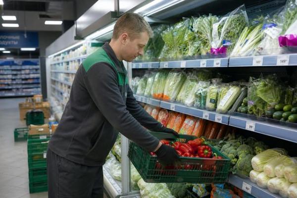 Сотрудник магазина загружает свежие продукты в холодильную горку в российском супермаркете Сотрудник магазина загружает свежие продукты в холодильную горку в российском супермаркете